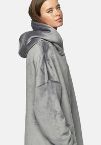 Un sweat à capuche gris surdimensionné en tissu pelucheux, doté d'une grande capuche, d'épaules tombantes et d'une texture douce. Design simple sans motifs.