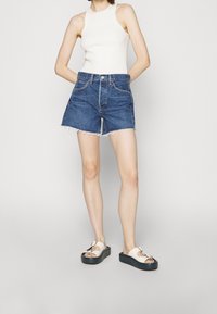 Siniset farkkuhameet, joissa on puretu reuna, yhdistettynä beigeihin platform-sandaaleihin, joissa on solk yksityiskohta. Viskoosikudottu valkoinen tankkitoppi viimeistelee asun.