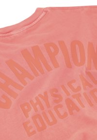 Camiseta de algodón rosa con letras naranjas en negrita que dicen "EDUCACIÓN FÍSICA CAMPEÓN". Textura suave y diseño de cuello redondo.