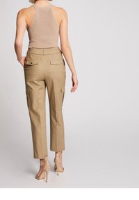Tan cargo bukser med tapered fit, featuring sidelommer og knap-lukkede baglommer, parret med en tætsiddende beige tank top og nude hæle.