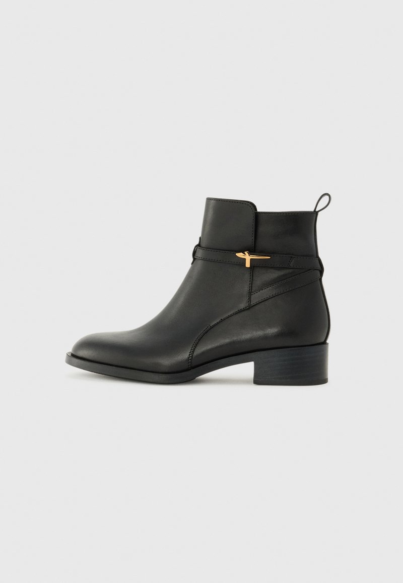 Černá kožená kotníková bota s nízkým podpatkem, s zlatým akcentem a zadním poutkem. Hladká textura a elegantní design.