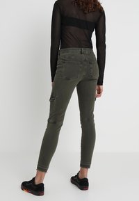 Olivgröna skinny jeans med hög midja, med cargofickor och fransad fåll. Svarta sneakers fulländar looken.