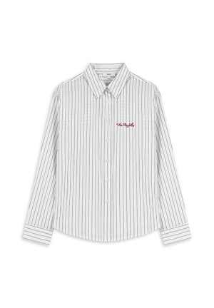 Chemise blanche à manches longues avec des rayures verticales noires. Elle possède un col pointu, une fermeture à boutons à l'avant, et un logo rouge brodé sur la poitrine gauche.