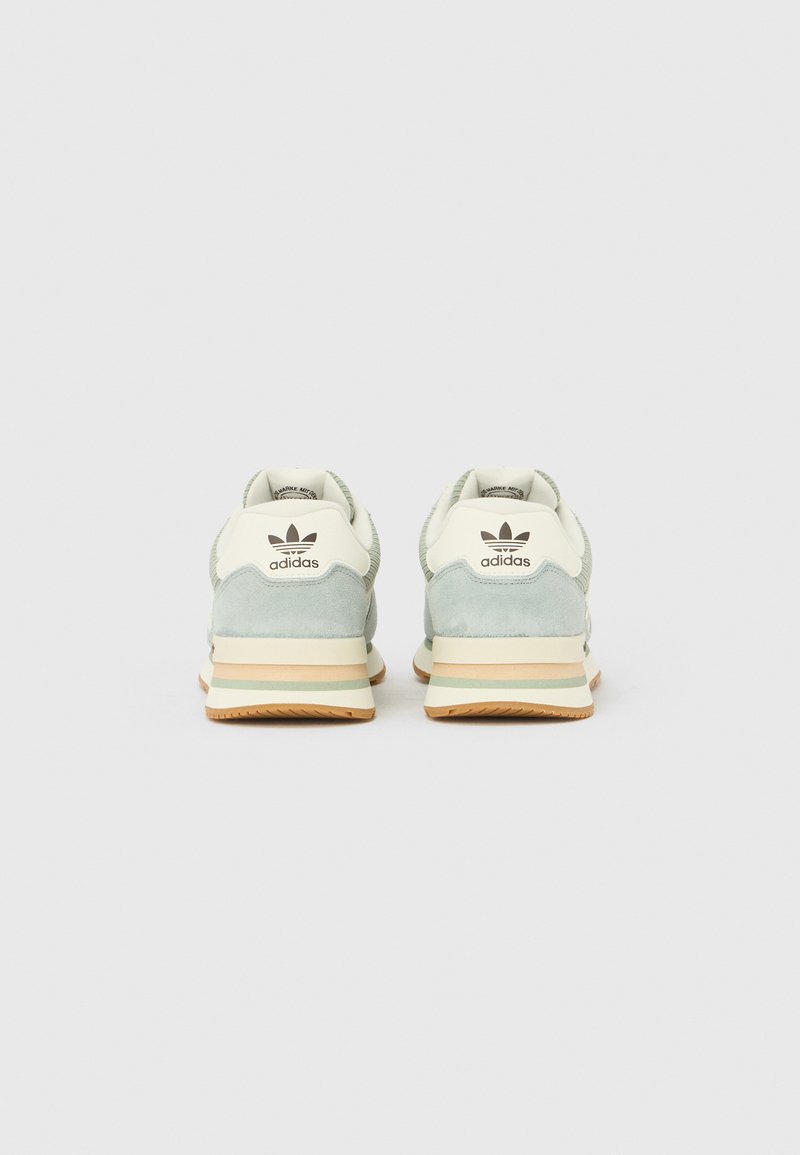 Paire de baskets Adidas vert clair et beige vues de dos sur un fond blanc.