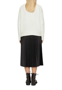 Cremfarbener, oversized Pullover mit langen Ärmeln, kombiniert mit einem schwarzen, plissierten Midi-Rock und klobigen schwarzen Schnürstiefeln.