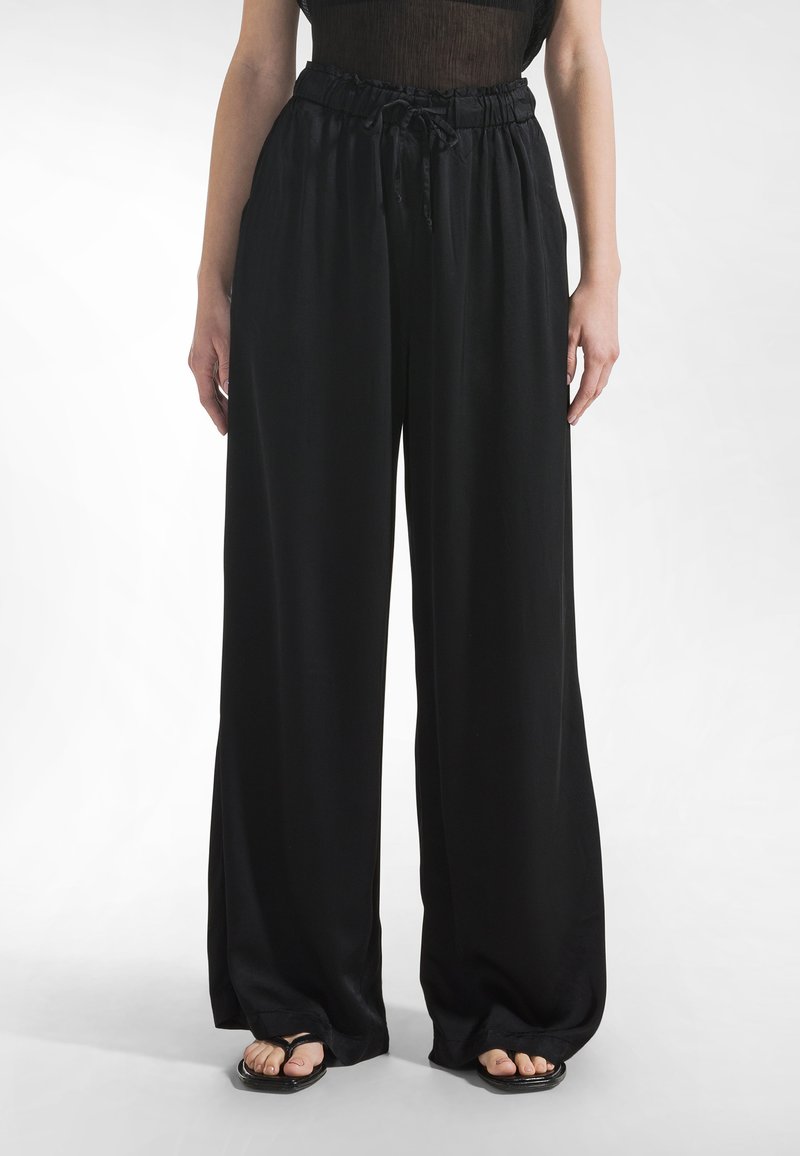 Mustat, leveälahkeiset housut, joissa on kiristysnauha vyötäröllä, valmistettu sileästä, kevyestä kankaasta. Housuissa on rento istuvuus ja hienovarainen kiilto.