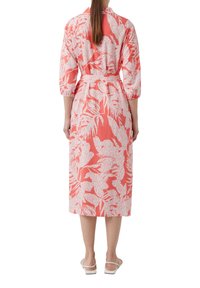 Koralowa midi sukienka z białym nadrukiem liści, luźny krój, kołnierzyk na guziki, rękawy 3/4, ściągnięta w talii i długość do kolan. Uwodzicielska tekstura.
