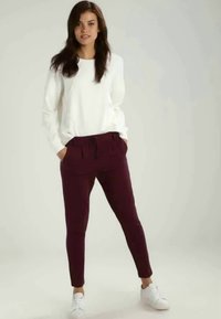 White long-sleeve top with textured sleeves, paired with fitted burgundy pants, featuring a drawstring waist and ankle-length fit, complemented by white sneakers.