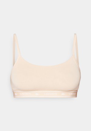 Lacoste-Bralette in hellbeige, glattes Material, Rundhalsausschnitt, dünne Träger, mit einem Logo-Band in kontrastierendem Hellbraun und Weiß.