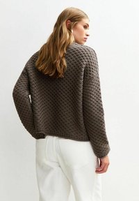 Bruin gebreid sweater met een textuurpatroon, voorzien van een losse pasvorm, lange mouwen en een verkorte zoom, gecombineerd met witte broek.