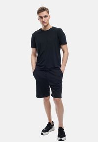Sort t-shirt med korte ærmer parret med sorte shorts, enkelt design, letvægtigt stof og en afslappet pasform. Sorte træningssko fuldender looket.