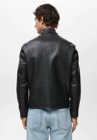 Giubbotto in pelle nera con un design aderente, dotato di colletto classico e polsini con zip, abbinato a jeans di denim blu chiaro.