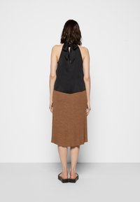 Musta satiini halter-top, jossa on solmimisnauha kaulassa, yhdistettynä ruskeaan neulottuun nilkkapituiseen hameeseen; mallilla on päällään mustat korkeat sandaalit.