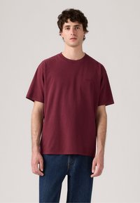 Bordeaux Baumwoll-T-Shirt mit kurzen Ärmeln, Rundhalsausschnitt und einem schlichten Design. Verfügt über ein minimales Branding auf der Brust.
