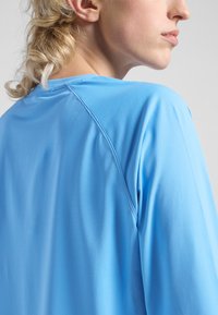 Lichtblauw, lange mouwen sporttop gemaakt van soepele, rekbare stof. Heeft een ronde halslijn en subtiele raglan naden.