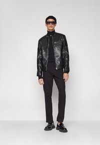 Black leather motorcycle jacket with silver zipper details, worn over a black turtleneck, paired with tailored black trousers and loafers.