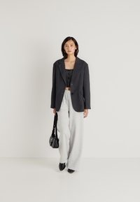 Μαύρο δομημένο σακάκι πάνω από ένα υφασμένο μαύρο crop top, συνδυασμένο με ανοιχτό γκρι φαρδύ παντελόνι φόρμας και μια μικρή μαύρη τσάντα.