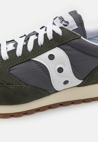 Zielone zamszowe i szare tekstylne trampki z białym logo, białymi sznurówkami i beżową gumową podeszwą, z kontrastowymi przeszyciami i oczkami.