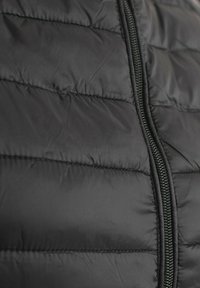 Chaqueta negra acolchada con un diseño acolchado, cierre central con cremallera y tirador metálico, y textura suave. Sin logotipos ni patrones visibles.