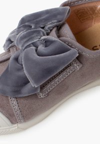 Sneaker in suede grigio con un grande fiocco in velluto grigio sul lato, suola in gomma bianca e dettagli di cucitura sottili.