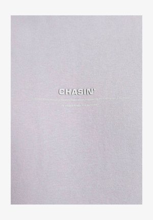 Svijetlosivi materijal s uzdignutim, reljefnim natpisom "CHASIN'" i sloganom ispod. Glatka tekstura i ujednačena boja po cijeloj površini.