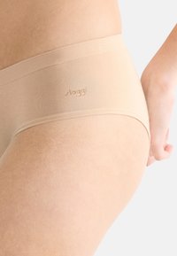 Slip beige clair en tissu lisse, avec une taille sans couture portant un logo de marque subtil. Le design offre une forme moderne et minimaliste.