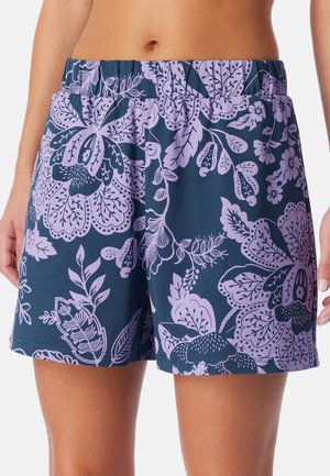 Femme portant un short bleu marine avec des motifs floraux violets clairs et une taille élastique, visible de la taille jusqu'au milieu de la cuisse.