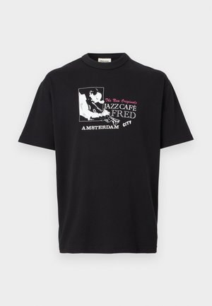 Fekete póló, rajta egy jazz zenészt ábrázoló grafika, amint trombitál, valamint a "Jazz Café Fred Amsterdam City" felirat fehér és rózsaszín színben.