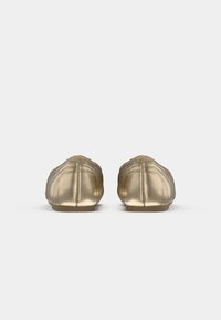 Chaussures slip-on métalliques dorées avec une texture douce, bout rond et détails cousus le long de la tige. Semelle plate.