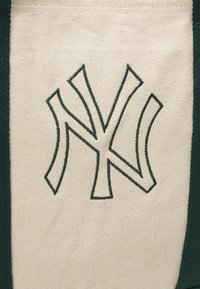 Sac fourre-tout en toile avec un fond crème et des accents vert foncé. Présente un logo "NY" brodé en vert foncé bien en vue.