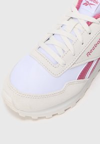 Tenisky Reebok v bielej a svetloružovej farbe, s vrchnou časťou z semišu a sieťoviny, okrúhlou špičkou, šnurovaním a textúrovanou gumovou podrážkou.