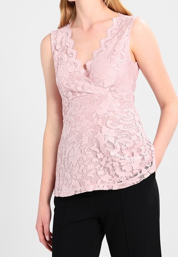 En rosa spetsblus med V-ringning, scallopade kanter och en figurnära silhuett, ihopparad med svarta byxor. Texturerad blommönster genom hela.