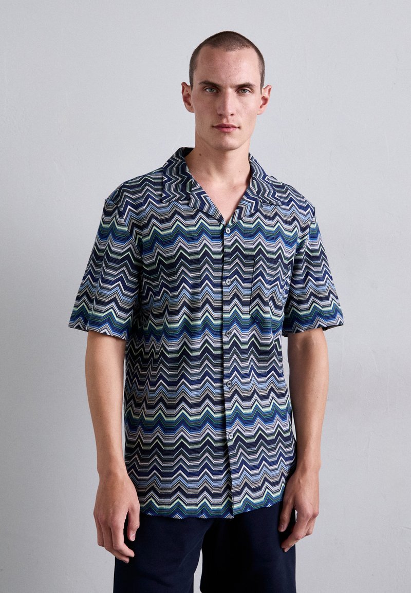 Camicia a maniche corte con un motivo a zigzag in blu, verde e nero. Realizzata in tessuto leggero con bottoni sul davanti.