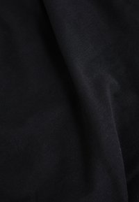 Svart bomullstyg med en slät textur som ger en subtil glans. Materialet faller mjukt utan synliga mönster eller detaljer i hårdvara.