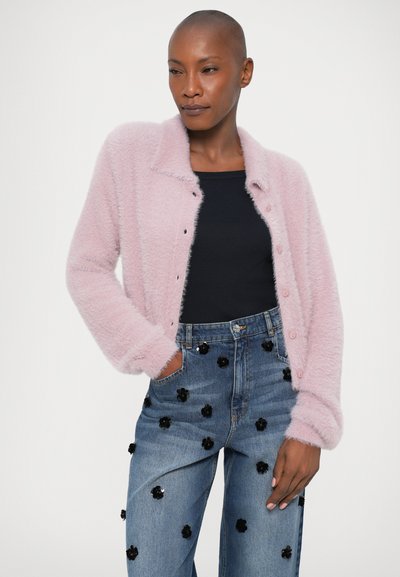 Svetloružový nadýchaný kardigán s golierom a gombíkmi, kombinovaný s modrými džínsami s čiernymi kvetinovými aplikáciami.