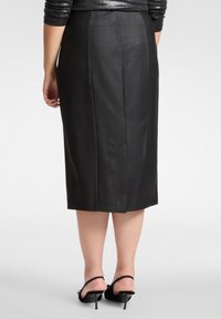 Czarna ołówkowa spódnica wykonana z gładkiego materiału przypominającego skórę. Długość do połowy łydki, z tylnymi szwami i dopasowanym krojem.