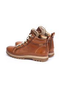 Tan leather hiking boots with gold hardware, padded collars, and a textured outsole. Features a high-top design and contrasting beige sole.