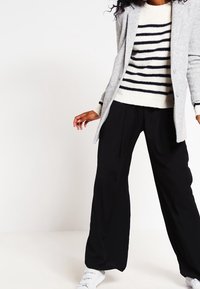 Cardigan grigio a maniche lunghe su un maglione crema con righe blu navy, abbinato a pantaloni larghi neri e scarpe da ginnastica bianche.