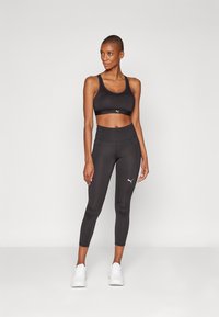 Svart sportsbh og leggings laget av elastisk stoff, med en tettsittende design, subtile logodetaljer og en glatt tekstur.