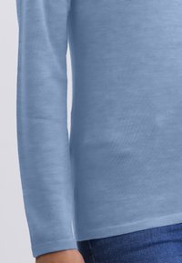Himmelblaues Langarmhemd aus weichem Stoff mit glatter Textur. Mit geradem Saum und schmalen Bündchen, getragen mit dunkler Denim.