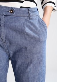 Světle modré džínové kalhoty s volným střihem, které mají přední kapsy, zapínání na knoflík a jemnou texturu. Spárovány s pruhovaným tričkem.