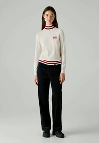 Kerimekoinen turtleneck-neule, jossa on punaiset ja laivastonsiniset raidat kauluksessa ja helmassa. Rinnassa on "Red Bull Racing" -logo. Yhdistetty mustiin housuihin.