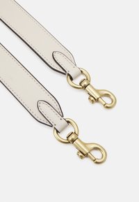 Cinturino in pelle color crema con bordi scuri a contrasto. Presenta clip e accessori in metallo dorato, che garantiscono durata e stile.