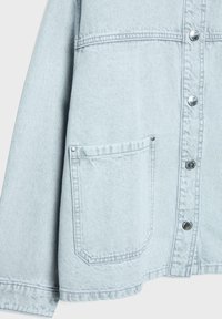 Lys blå denimjakke sektion med ærme, forlomme og fire synlige sølvknapper med syningsdetaljer.