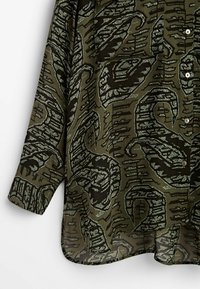 Green patterned shirt featuring an abstract black and metallic grey design, with a button-up front and long sleeves. Light, textured fabric.