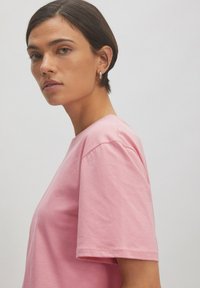 Rosa Baumwoll-T-Shirt mit lockerer Passform, kurzen Ärmeln und rundem Ausschnitt. Glatte Textur ohne sichtbare Muster oder Hardware-Details.