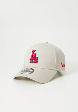Beige baseball cap with an embroidered red and blue "LA" logo on the front. Features a curved brim and adjustable strap at the back.
