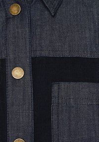 Veste en jean bleu foncé avec des boutons dorés, un tissu texturé et des coutures visibles sur la poche avant.