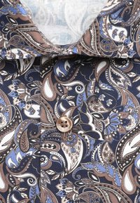 Gros plan d'un col de chemise et d'un bouton avec un motif paisley détaillé en bleu, marron, blanc et noir.