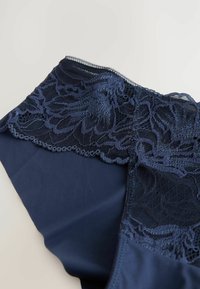 Marineblaue Unterwäsche mit einem floralen Spitzenbesatz am oberen Rand und einem glatten Satin-Finish am Körper. Weiche Textur mit filigranen Details.